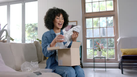 Mujer-Birracial-Feliz-Desempacando-La-Caja-De-Compras-En-Casa,-Cámara-Lenta