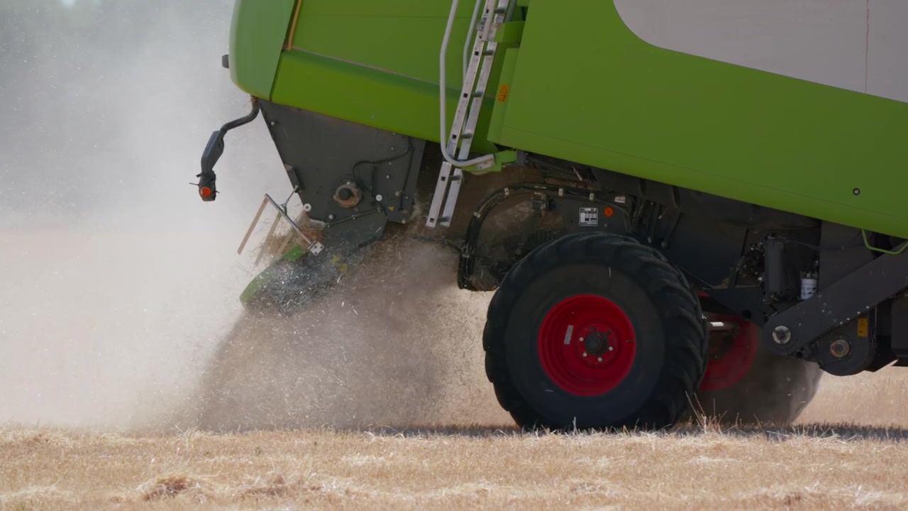 Close up of a green combine harvester working in a wheat field in slow motion, expelling chaff and kicking up dust