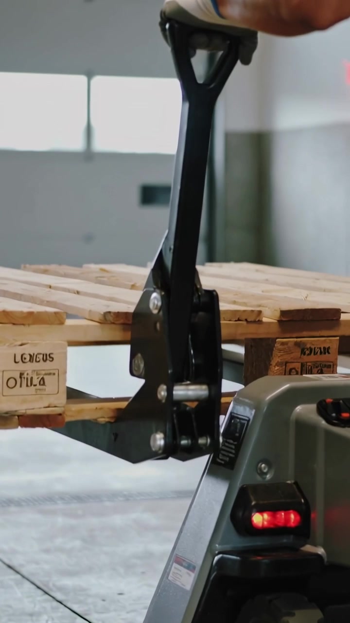 Video verticale: Lavoratore guantato che tira la maniglia di un transpallet al molo, sollevando il pallet per spostarlo.