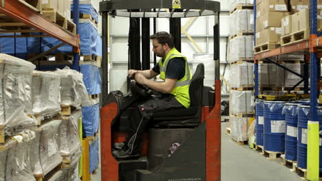 young male warehouse worker sits into forklift and drives away, static view