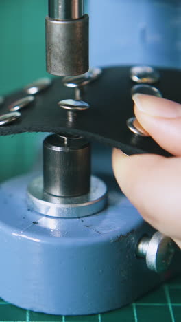 cu: skilled worker fixes silver holnitens on stylish black leather choker on green mat in tailor workshop closeup