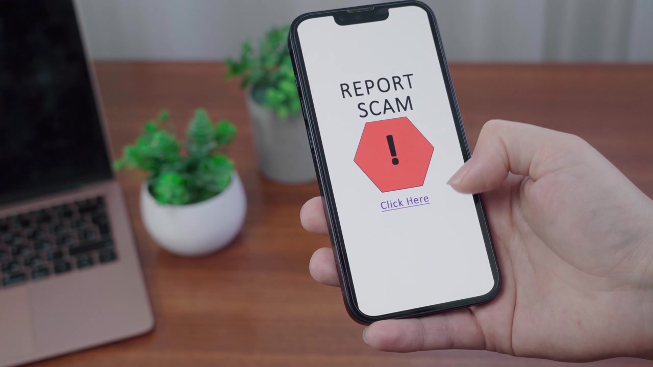 Hand holds a mobile device with an AI information alert inviting the user to report a scam by tapping a warning icon.