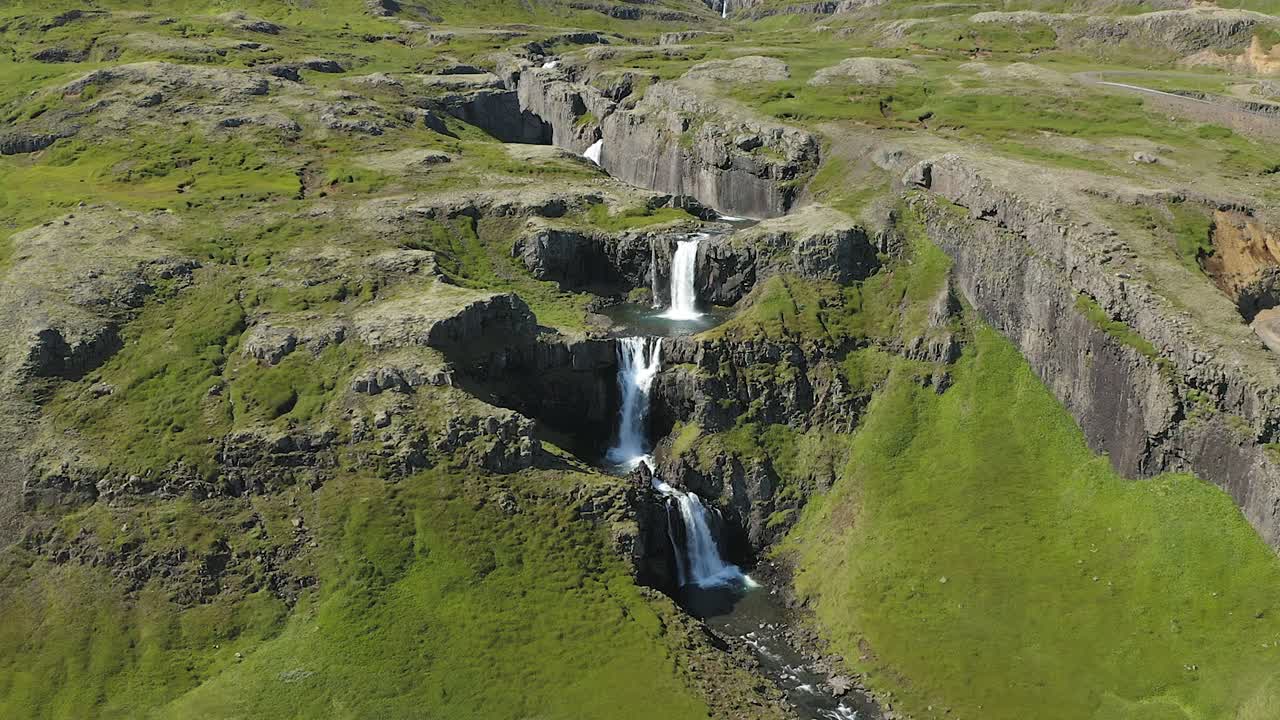 Klifbrekkufossar waterfall in Iceland. Flight forward, tilt and zoom in. Mossy and rocky green mountain landscape. Nordic nature.