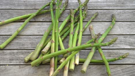 Slow-motion-footage-of-a-bunch-of-fresh,-green-asparagus-falling-on-to-a-wood-table