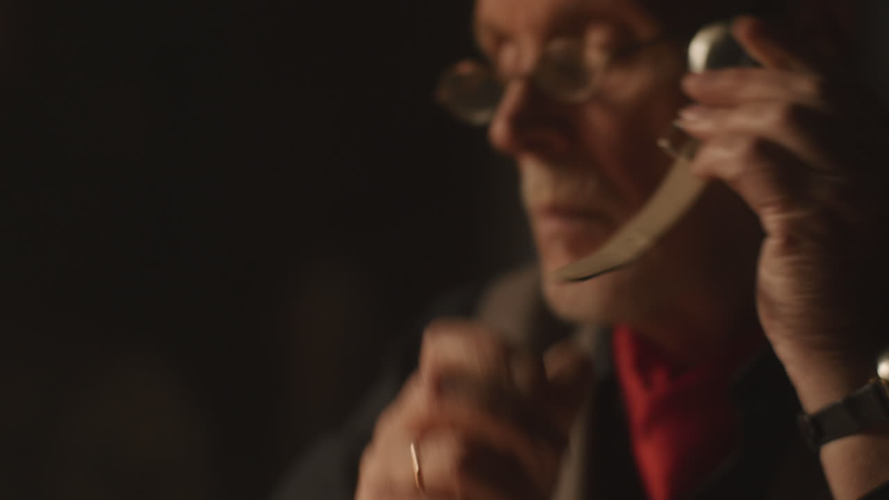 Older passionate man evaluates an old watch in his office at night