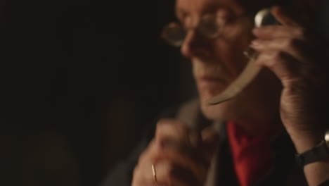 older passionate man evaluates an old watch in his office at night