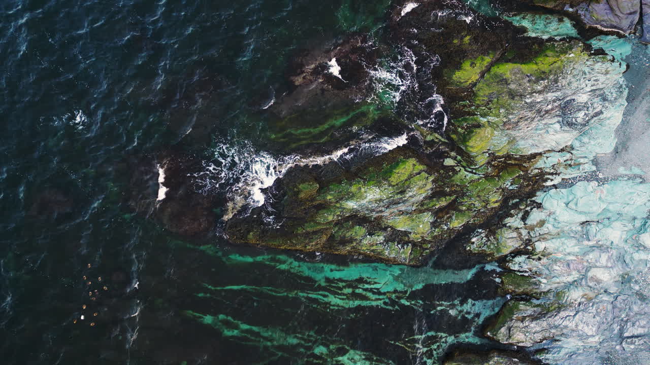 Drone top down ascends above ocean waves crashing on tendrils of white rock with algae