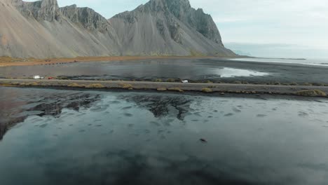 Drone-tilt-up-over-black-sand-Stokksnes-beach-revealing-Vestrahorn-mountain