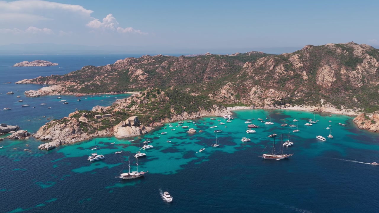 Large vue aérienne d'ensemble de yachts à voile de luxe dans une eau bleu turquoise, avec une magnifique plage de sable nichée dans des falaises de granit sur l'île de Spargi dans l'archipel de la Maddalena en Sardaigne, Italie.