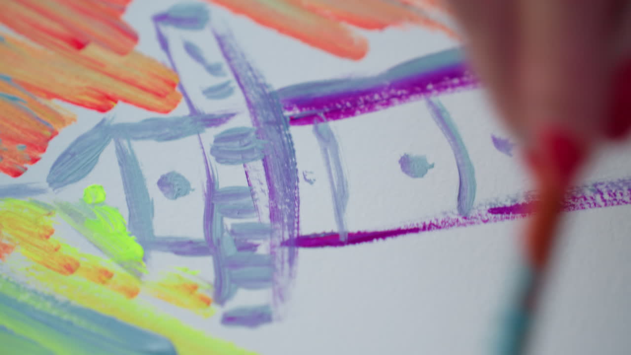 close up creative hand painting tall tower outline with purple and blue watercolor on white sheet while applying bold orange and red behind strokes on paper placed on wooden surface by river sunset