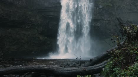 huge waterfall on free flowing river after heavy rainfall with logs and cliff in wales uk