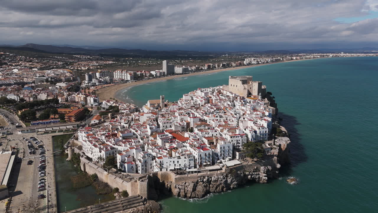 Castell de Peniscola above waterfront with curved marina bay and town in golden sunlight