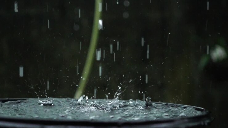 Heavy rain water droplets falling into water barrel, slow motion closeup