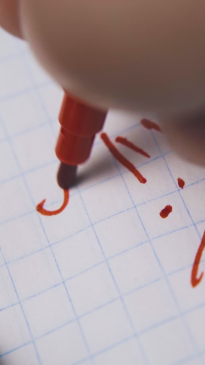 young man writes exclamation marks with red marker on blank checkered paper sheet extreme close view