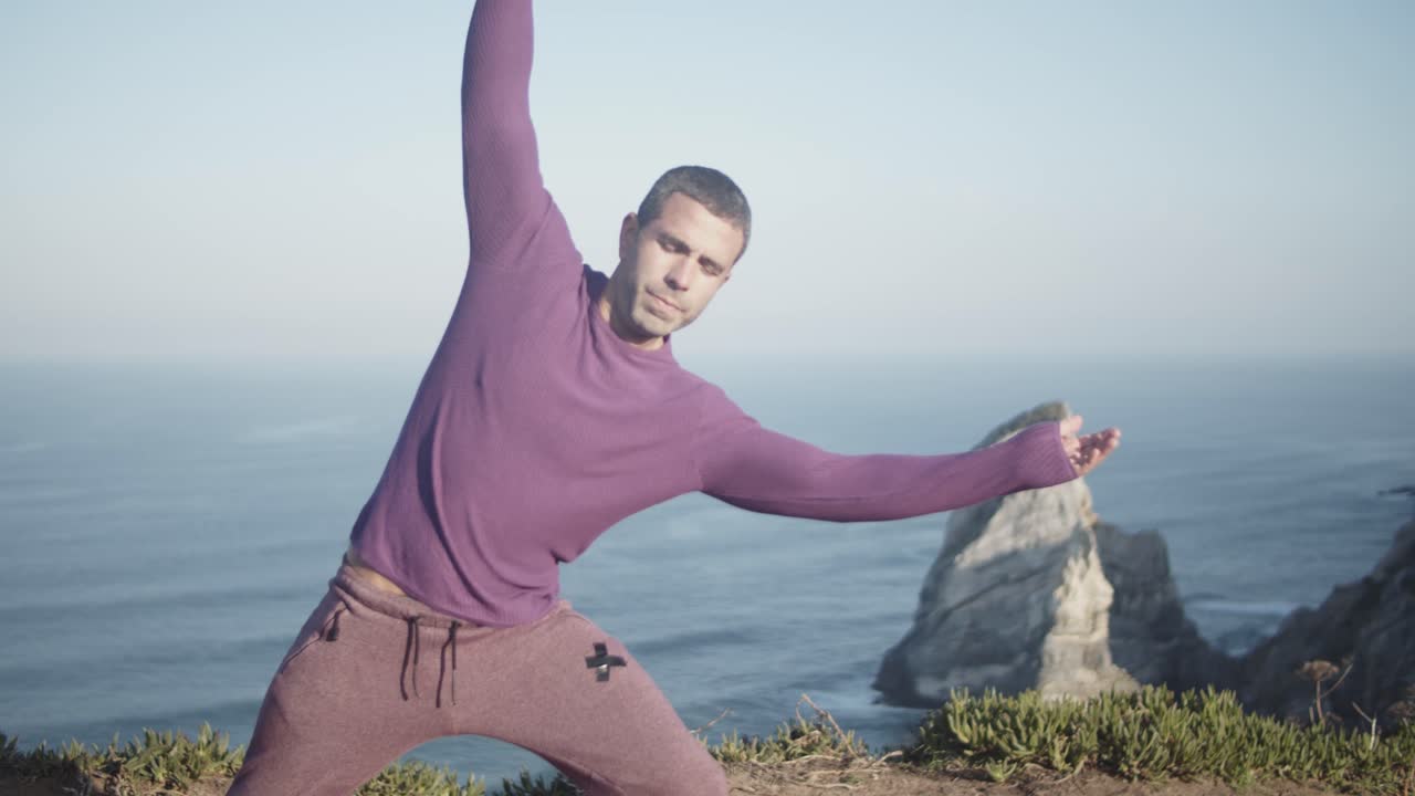 Man in casual activewear doing standing side stretch on scenic cliff above Atlantic Ocean at Praia da Marinha in Algarve, Portugal with golden rocks and calm sea in background on clear day
