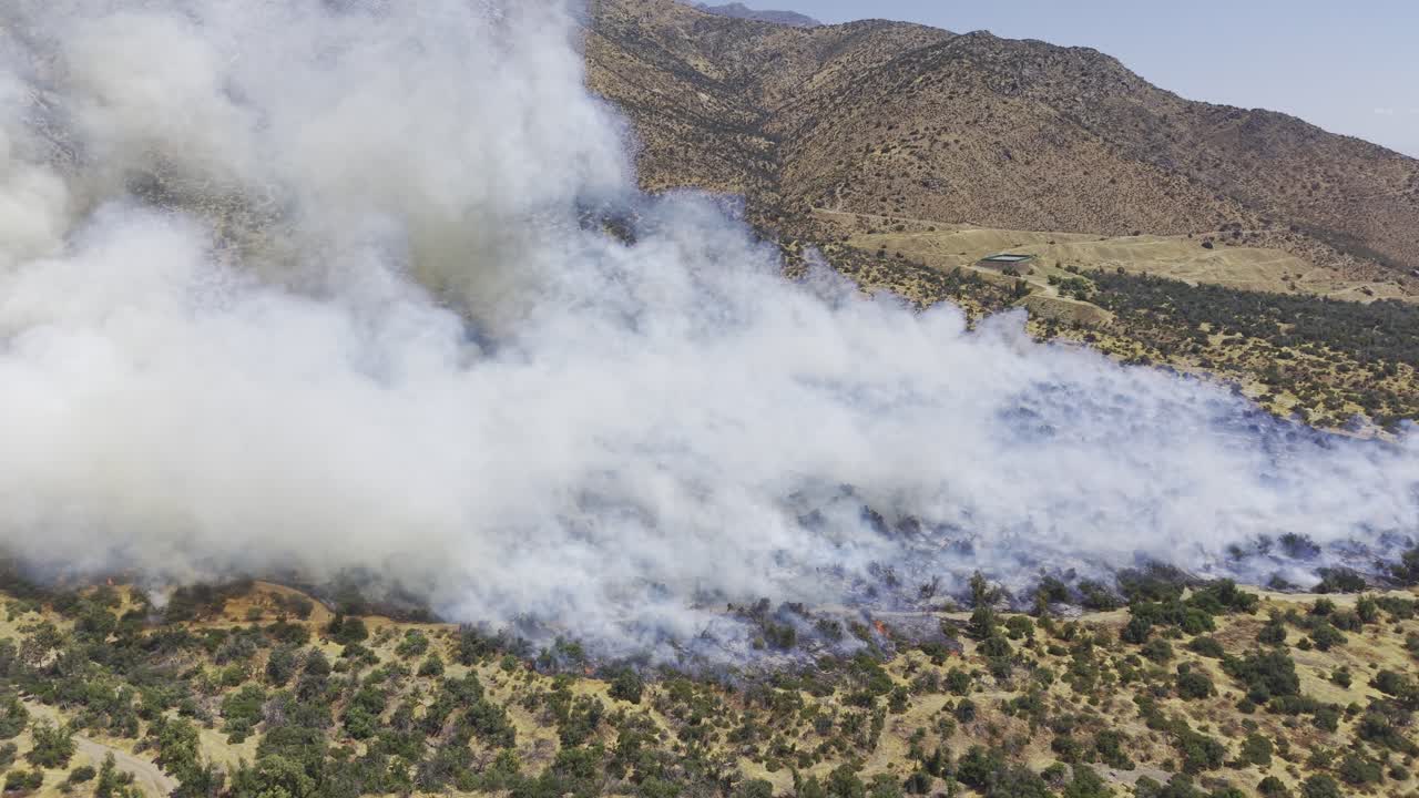 And Dağları, Şili’de bir dağ yamacında bitki örtüsünü yakarak kalın duman çıkaran bir yangının sinematik hava drone’uyla çekilmiş geniş açılı görüntüsü, 4K