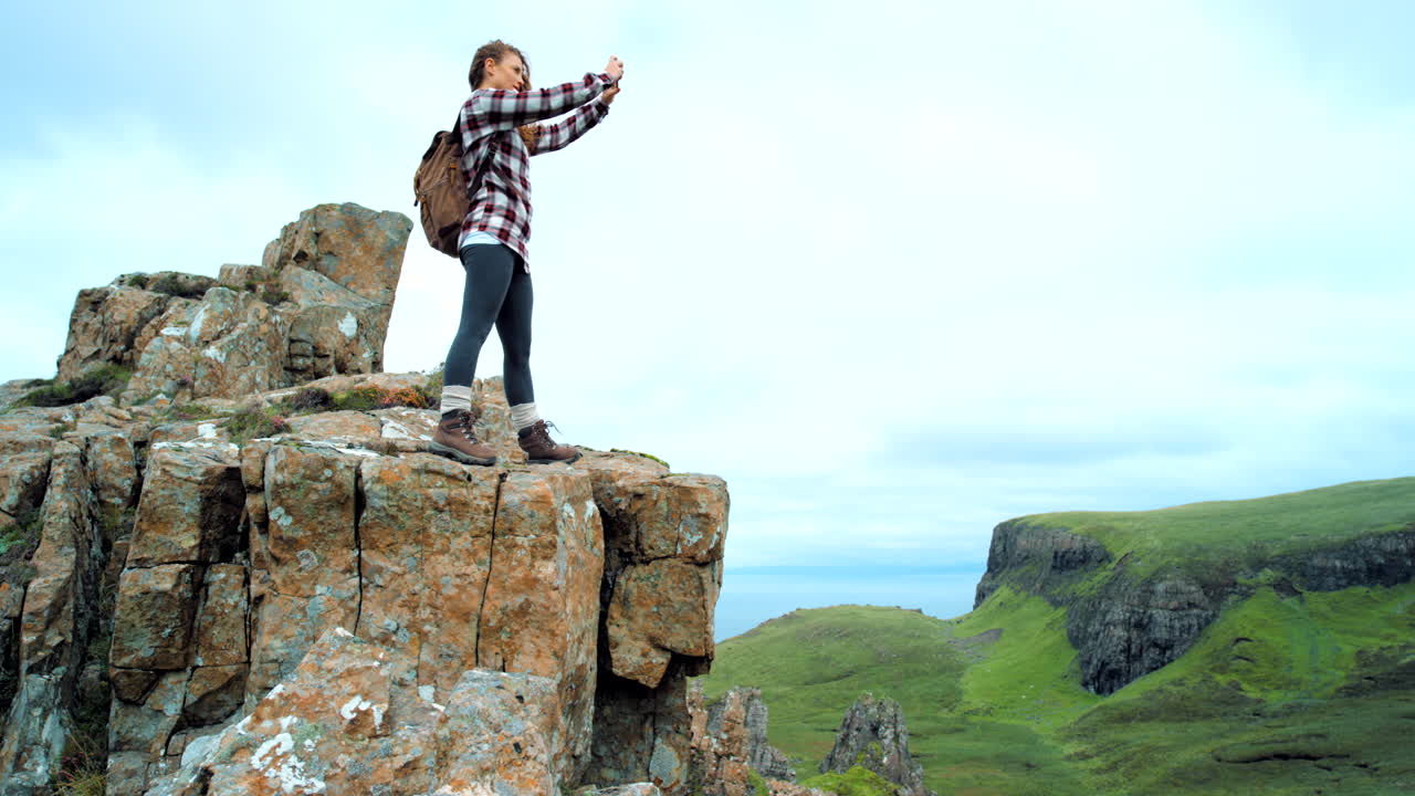 mujer caminando por un acantilado de montaña tomando fotos