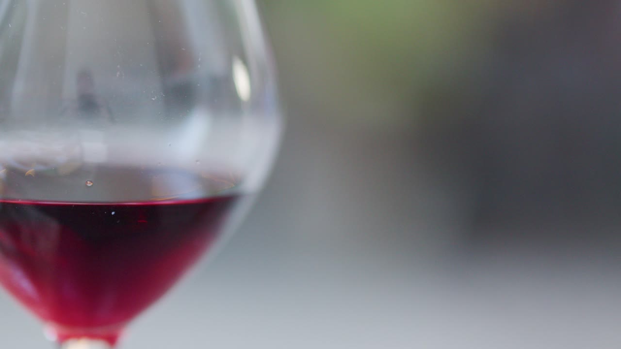 Close-up of red wine glass, shallow depth of field, gentle camera movement, blurred dining background