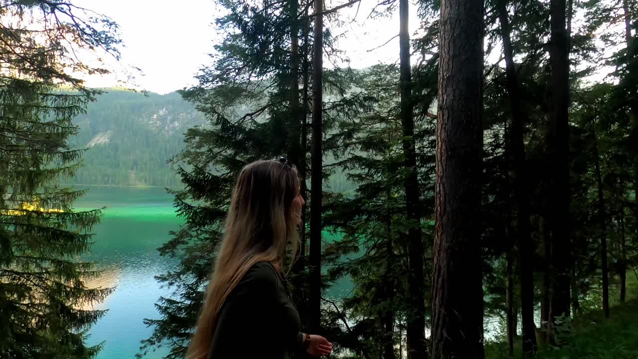 White girl with blonde hair, wearing a green top and sunglasses, walks next to the famous lake Eibsee in Germany