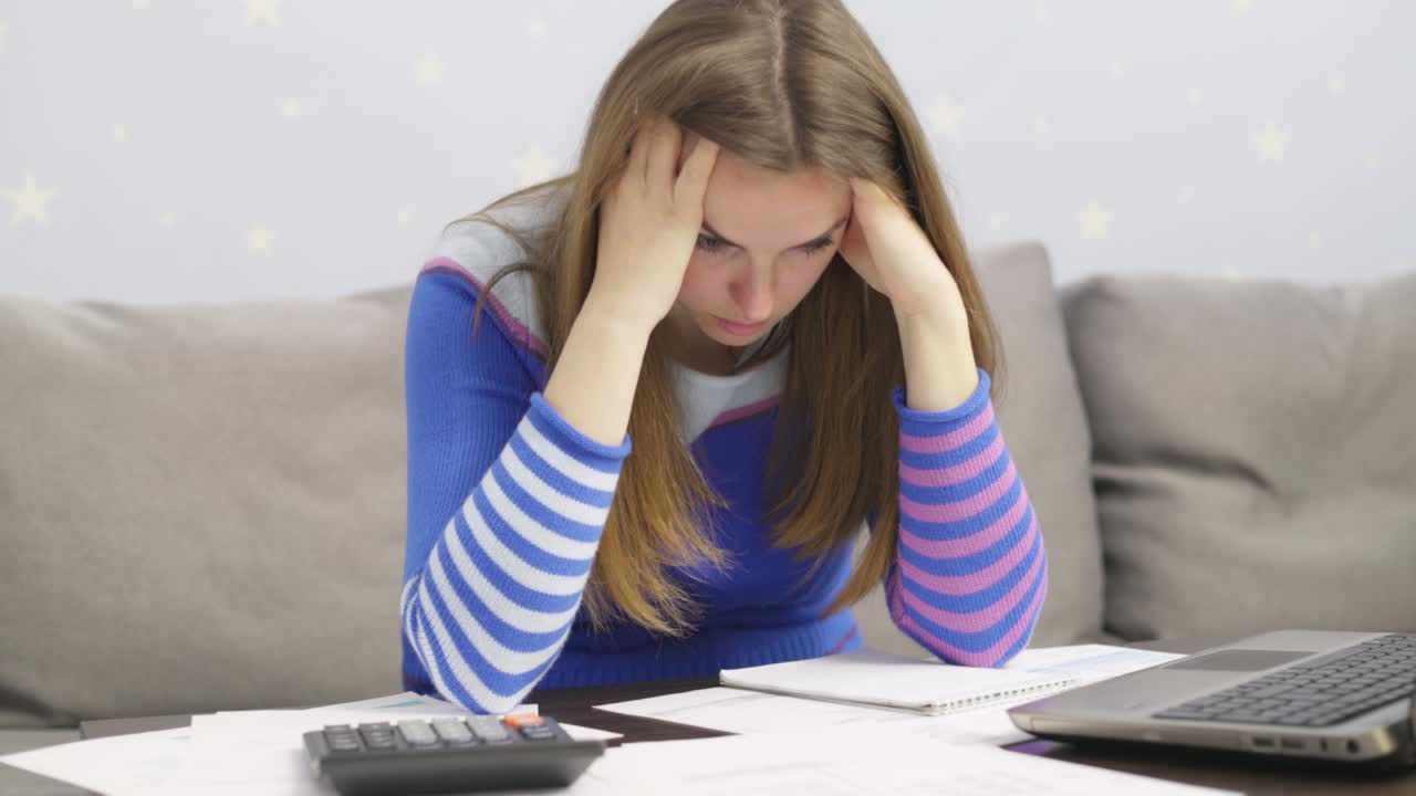 Stressed young brunet woman sits at home manage household finances frustrated with family financial problems. Distressed upset female disappointed with money debt, pays bills taxes online on laptop