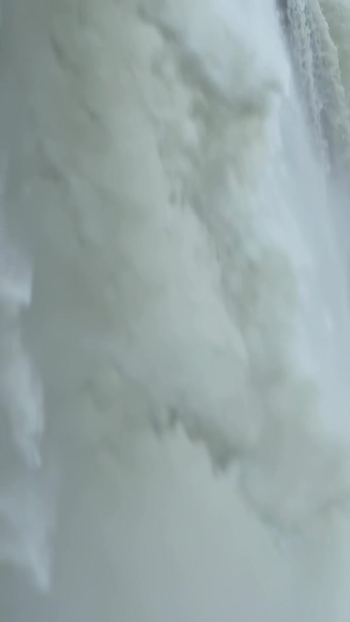 Video verticale: Cascata impetuosa che si riversa da uno sfioratore dopo un forte rilascio, generando schiuma e nebbia.