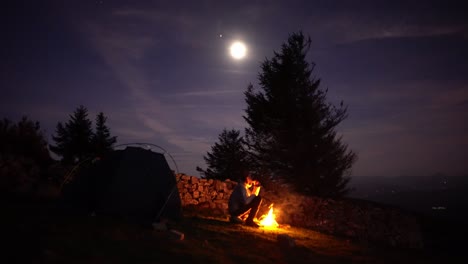 hombre come solo en la hoguera del campamento de tiendas con luz de luna llena en el desierto