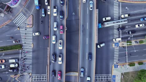 ascending overhead shot moving away from a busy intersection, revealing pedestrians crossing and vehicles in motion, all captured in daylight to highlight urban activity and movement