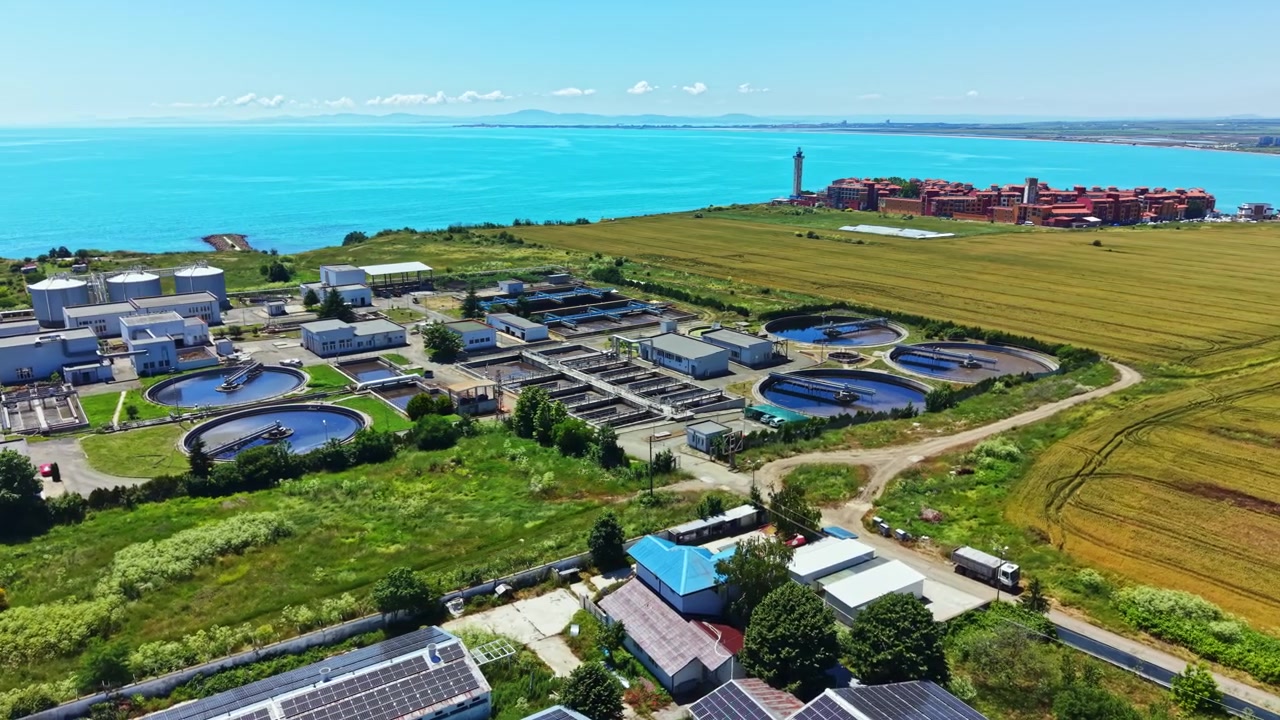 Water treatment facility beside the shoreline with blue water, fields, and buildings under clear sky during day