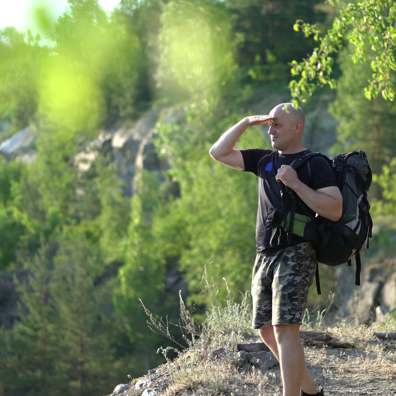 Hiker male looks at the beautiful landscape on the natural green background. A tourist man with a rucksack standing on the hill and admires the nature in a sunny day