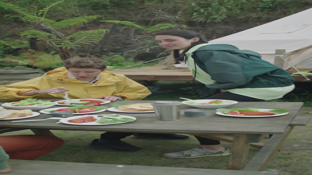 Friends Serving Dinner on Wooden Table while Glamping