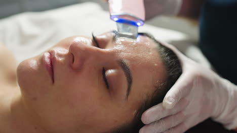 female spa therapist in protective gloves using professional extraction tool to gently remove pimples from client face during precise acne treatment, showcasing close up skin care procedure