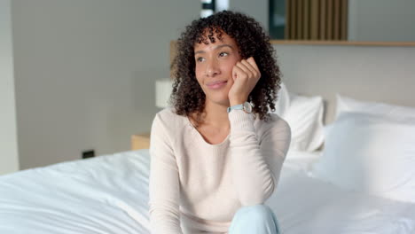 sitting on bed, woman with curly hair daydreaming and smiling softly