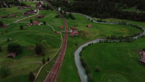 aerial tilt up over railway tracks revealing an impressive valley of towering mountains in switzerland