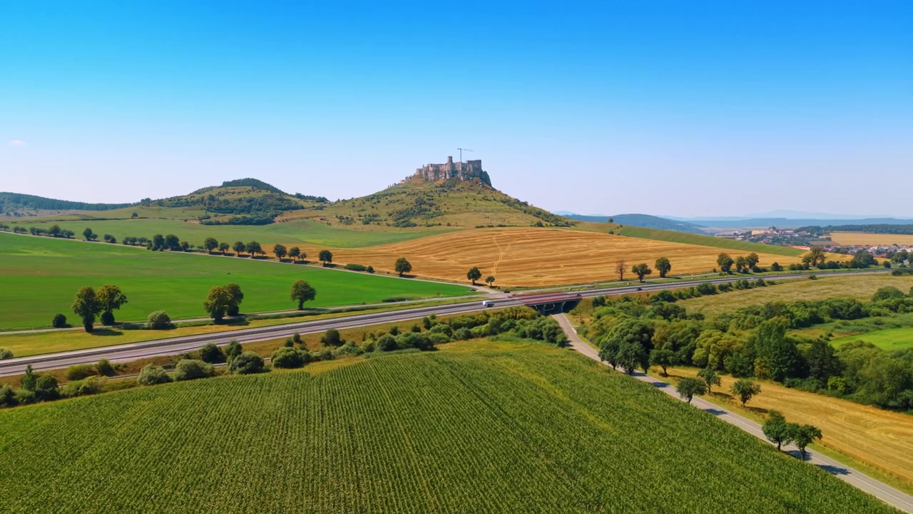 Uitzicht op heuvels met een kasteel en velden. Luchtfoto van glooiende heuvels met een kasteel erbovenop. Groene velden en wegen strekken zich uit over het landschap.