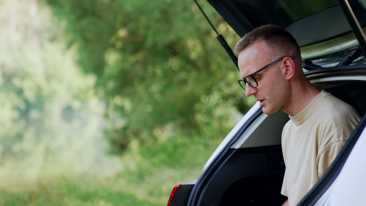 Working in nature. Man in glasses types on his laptop, speaking to himself. Freelance concept.