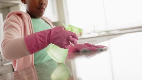 happy african american girl cleaning countertop in kitchen, in slow motion