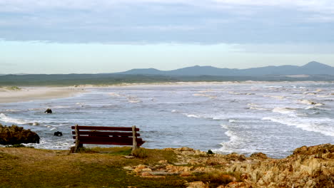 en un banco panorámico de la costa de hermanus con vistas a la gruta, la playa de la bandera azul y las olas.