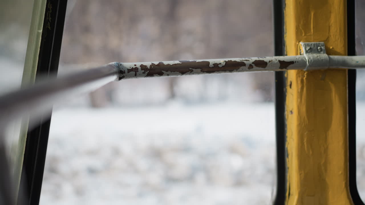 close side view window handle on moving train, chipped paint metal bar by glass, winter blur outside with snow and trees, gentle vibration and soft daylight across yellow frame