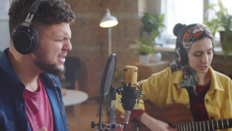hombre cantando una canción mientras la mujer toca la guitarra en el estudio de grabación