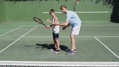 caucasian father teaching his son to play tennis at tennis court on a bright sunny day