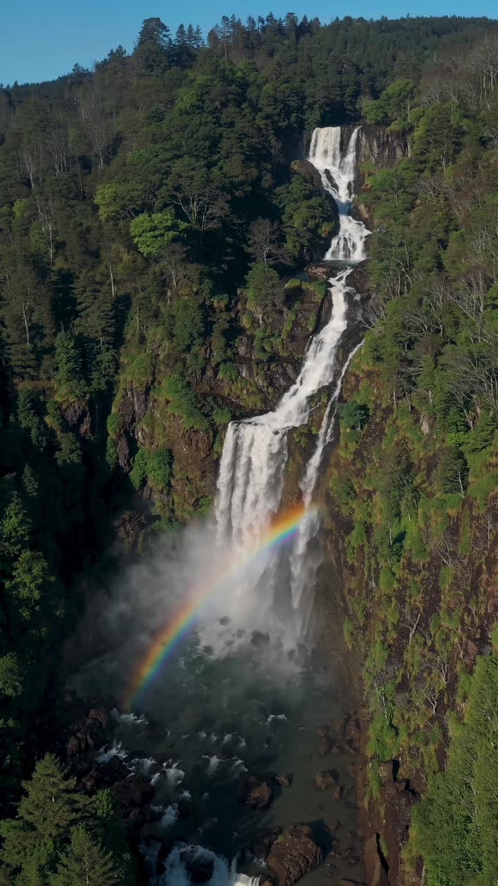 Aerial view of a cascading waterfall with a rainbow, surrounded by lush forest