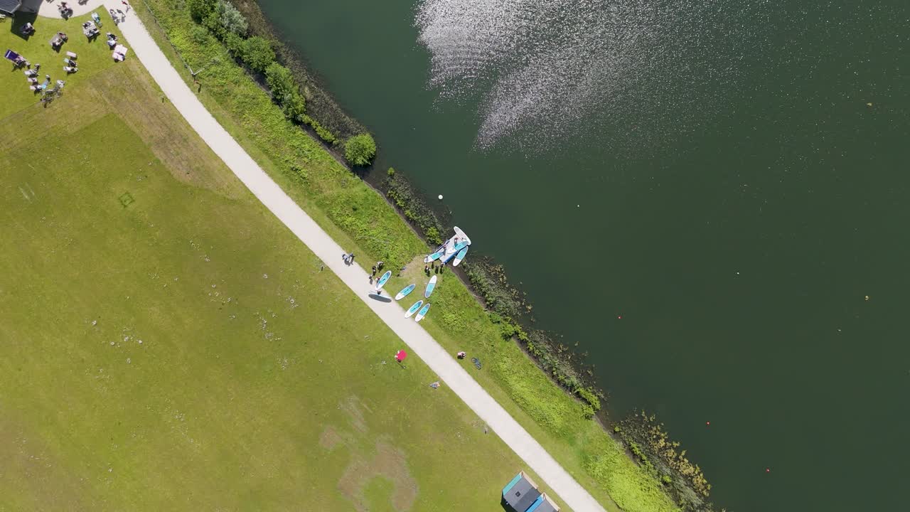Drone footage capturing a top-down view of kayakers launching into a calm lake surrounded by lush greenery. Ideal for outdoor, water sports, and nature footage.
