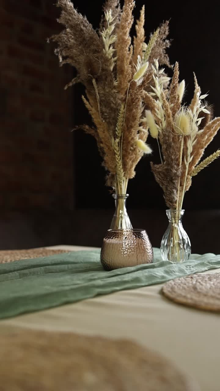 Mano che posiziona un portacandele su un tavolo con composizione floreale secca