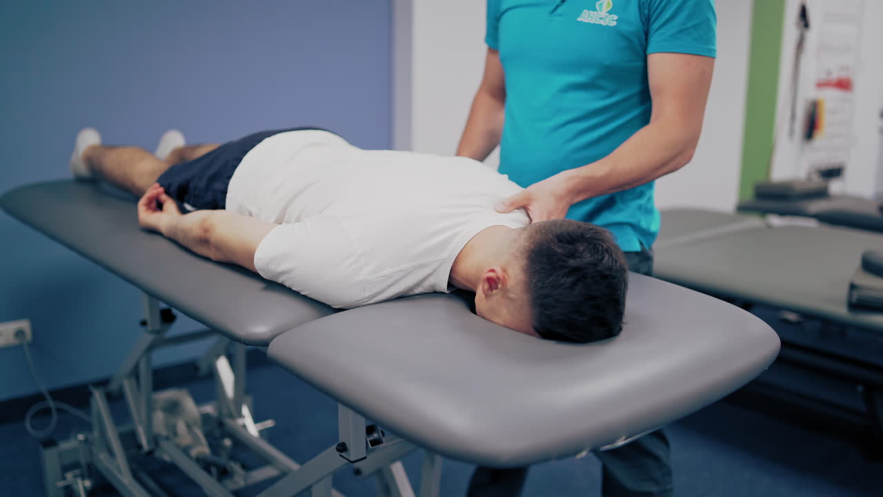 Man in white t-shirt is having a neck massage in spa center. Professional massagist is doing therapy treatment on a man's body indoors.