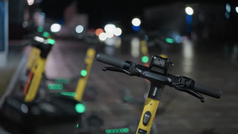 blurred view of parked electric scooters with distinctive night lights in the background, with soft bokeh effects from the streetlights