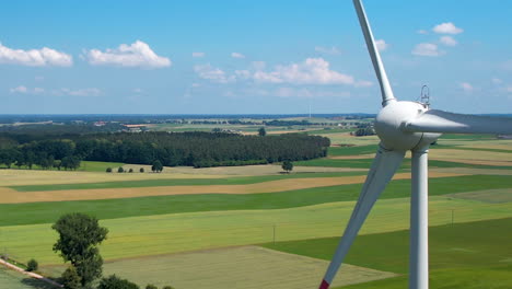 Close-up-of-a-wind-turbine-spinning-over-farmer's-fields-on-sunny-summer-day---aerial
