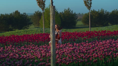 una joven irreconocible tocando el violonchelo en un campo en flor en primavera.