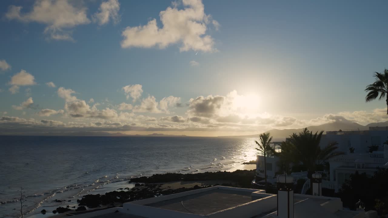 Sunset over the ocean beach with buildings and palm trees