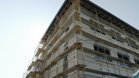 building under construction with scaffolding and workers on a sunny day