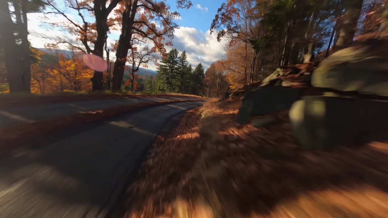 Approaching right-hand curve, camera capturing winding road through autumn woods with leaf piles